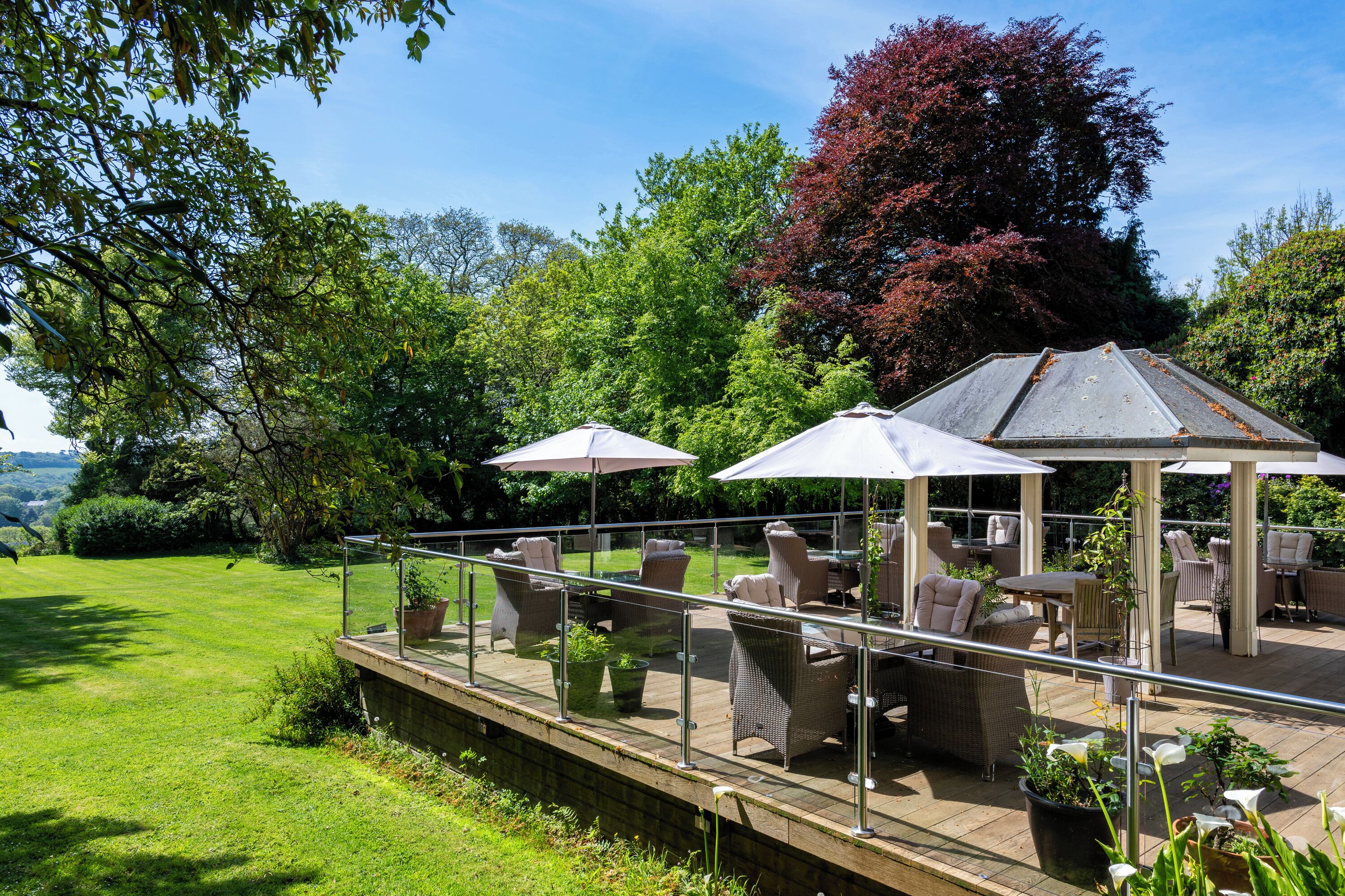 An outdoor patio with wicker furniture, umbrellas, and potted plants.