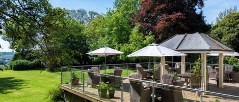 An outdoor patio with wicker furniture, umbrellas, and potted plants.