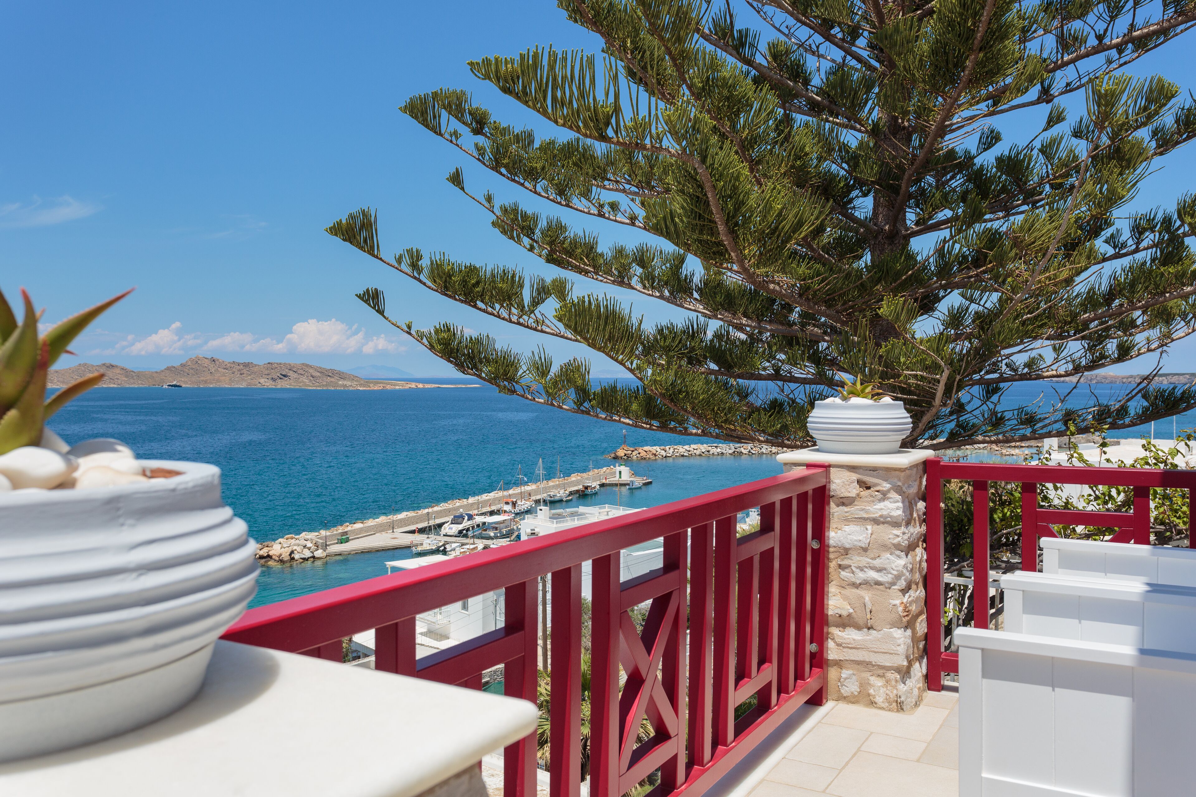 Un balcon avec une balustrade rouge donnant sur une marina et la mer.