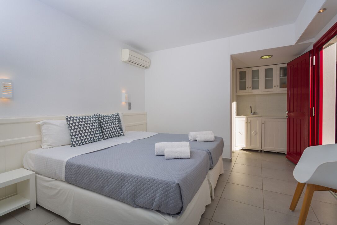 Una habitación de hotel con cama, mesitas de noche, escritorio y kitchenette.
