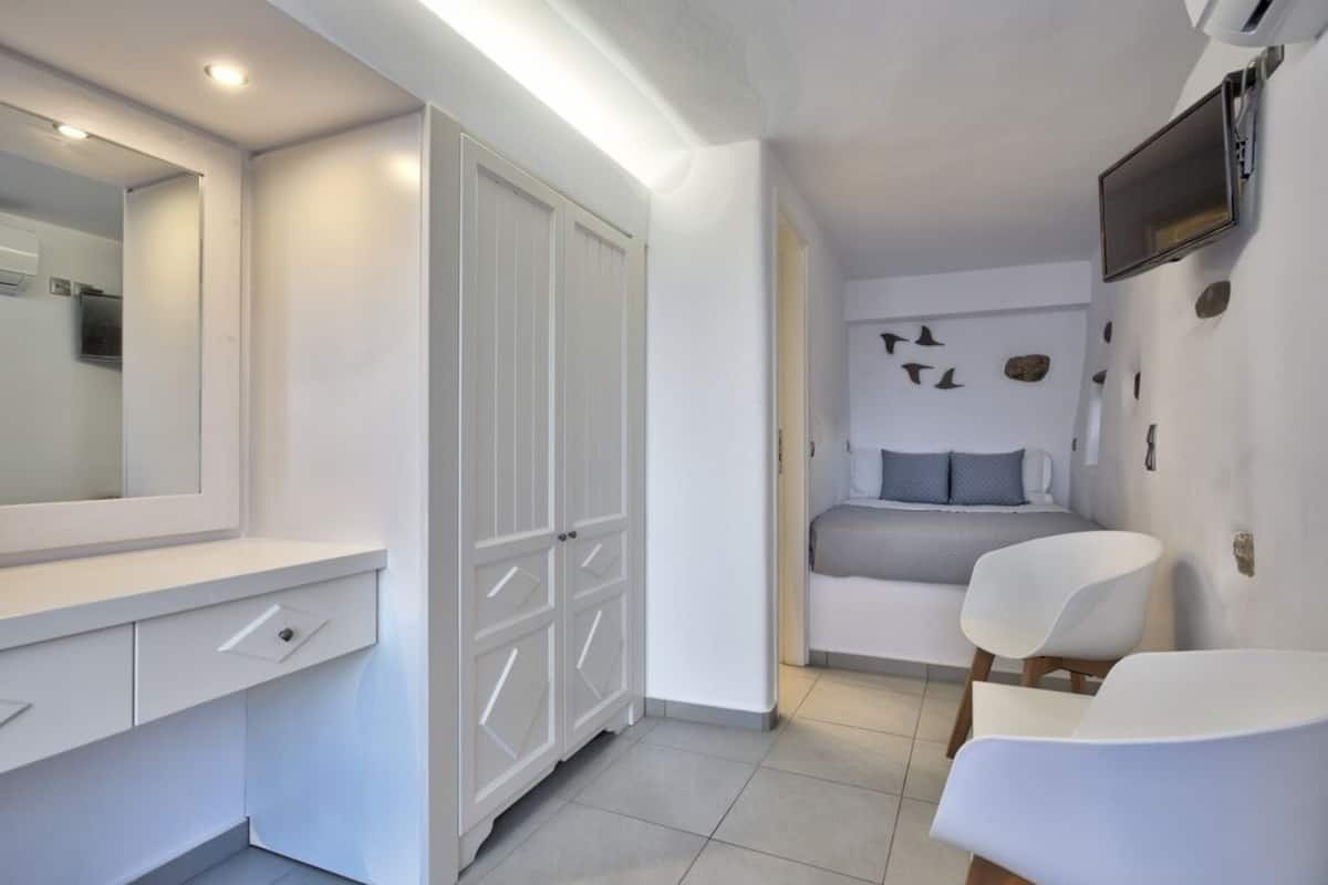 A modern bedroom with a bed, a large mirror, a wardrobe, and a TV mounted on the wall.
