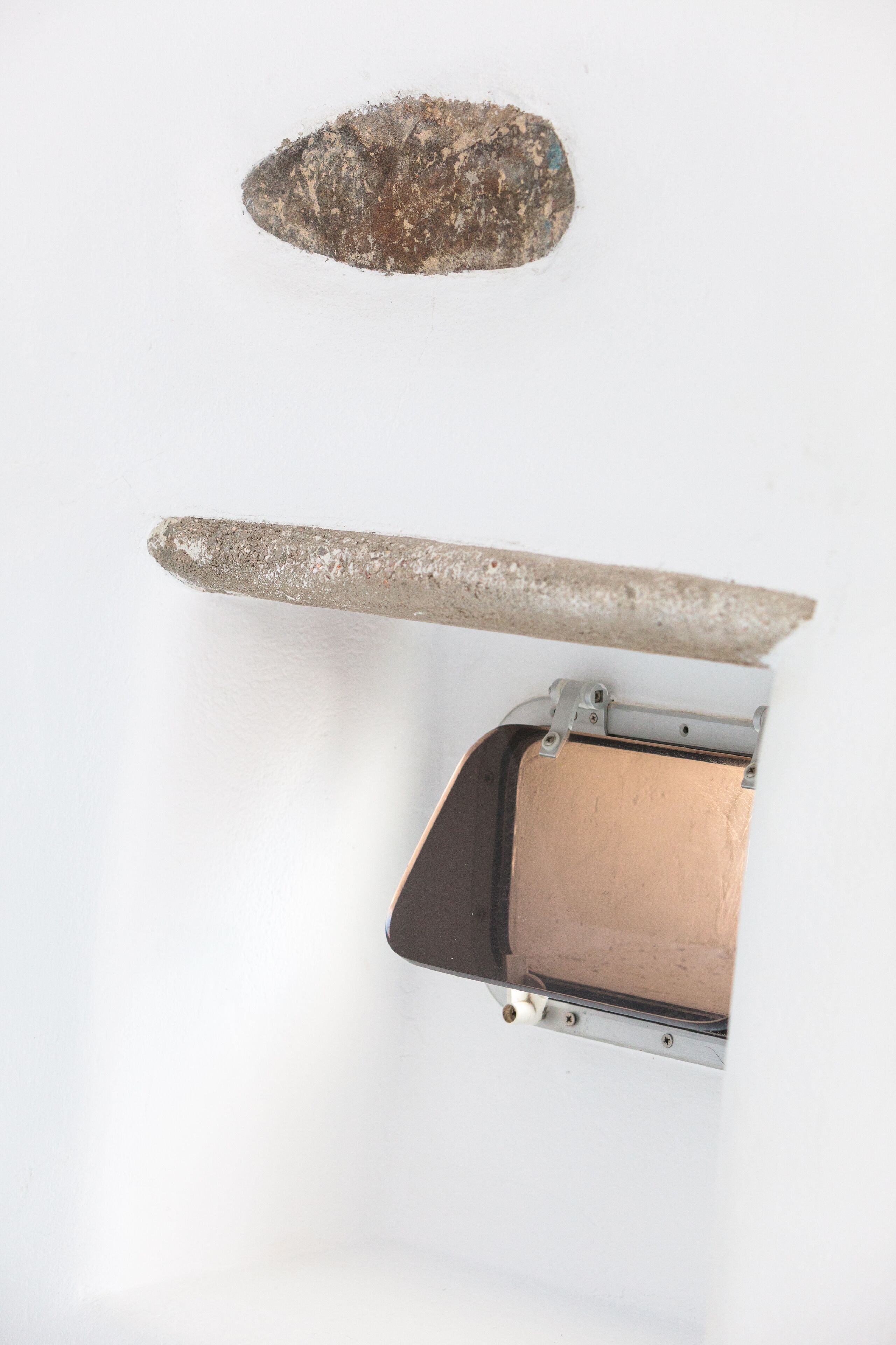 A wall with a recessed shelf, a stone-like object, and a metallic object.