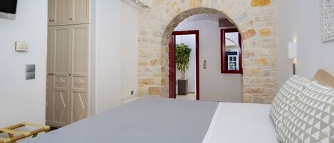 A bedroom with a bed, a wardrobe, a stone wall, and an arched doorway.