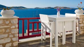 A terrace with a white table and chairs, potted plants, and a red railing overlooking a body of water.