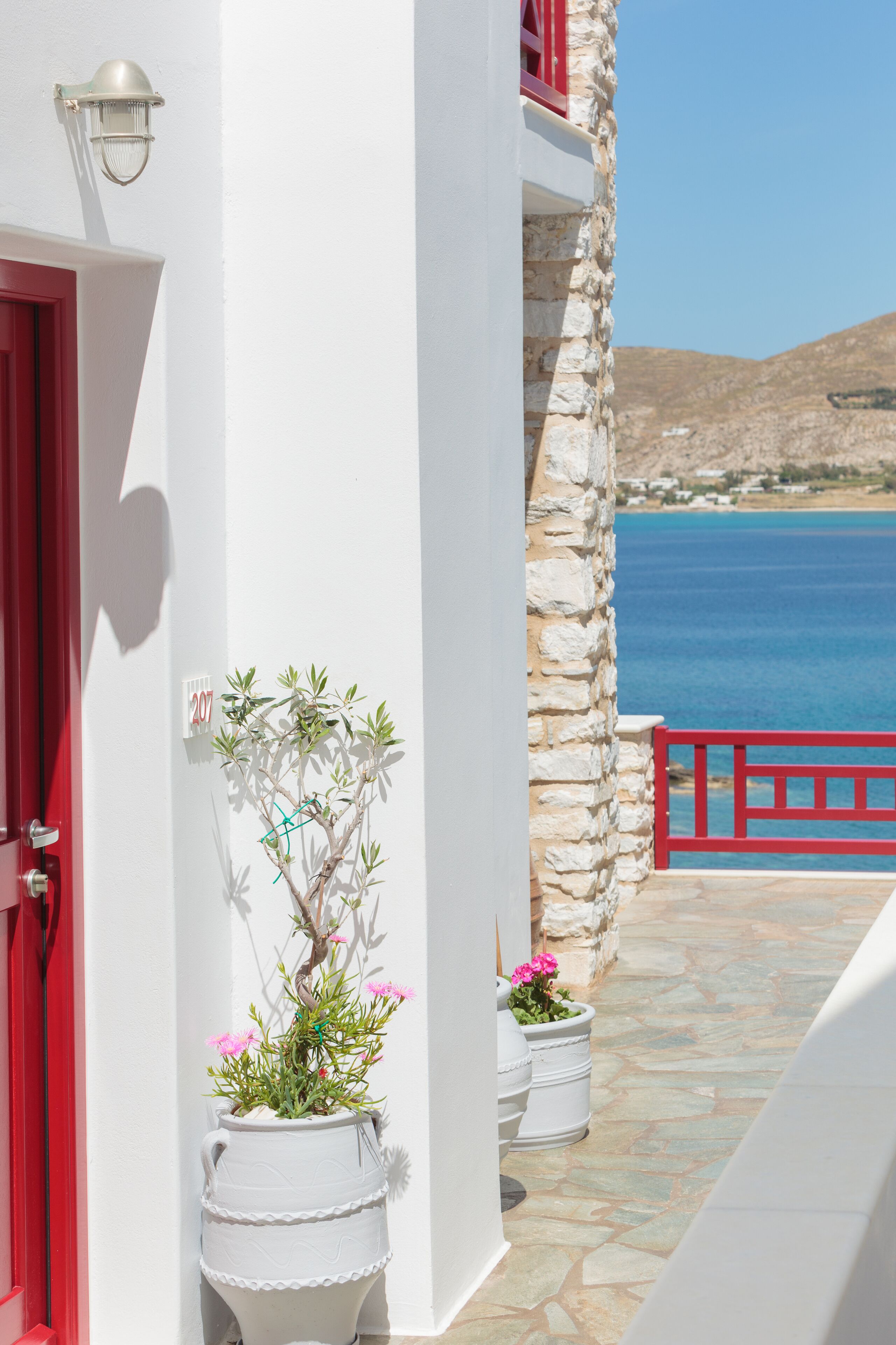 Un edificio blanco con puerta roja y balcón que da a un mar azul.