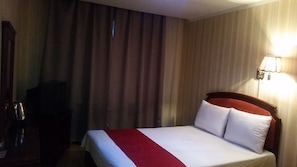 A hotel room with a bed, curtains, a lamp, and a television.