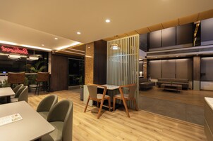 Un interior de restaurante moderno con suelo de madera, una zona de comedor con mesas y sillas, una barra y una sala de estar con sofás y una mesa de centro.