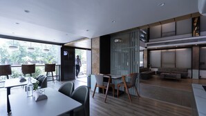 A modern restaurant with a wooden floor, grey chairs, and tables. There is a large window with a view of greenery outside. - Pride Biznotel Alkapuri (Vadodara)
