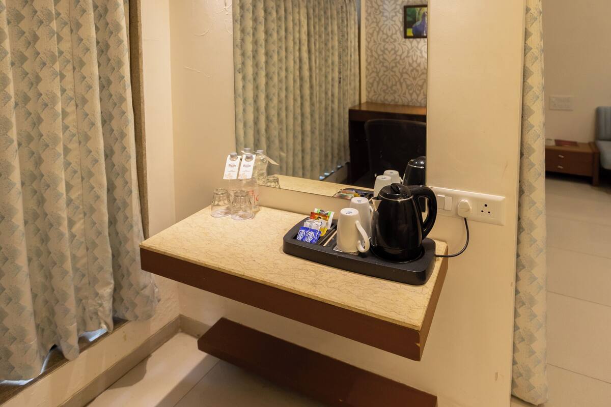 Quarto de hotel com escrivaninha integrada, espelho, cafeteira e televisão.