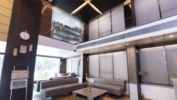 A modern interior with a high ceiling, a seating area with sofas, a coffee table, and a large window. - Pride Biznotel Alkapuri (Vadodara)