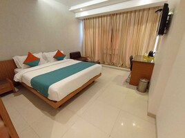 Habitación de hotel con cama, escritorio, silla, cubo de basura y ventana con cortinas.