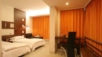A hotel room with two beds, a desk, a chair, and orange curtains.
