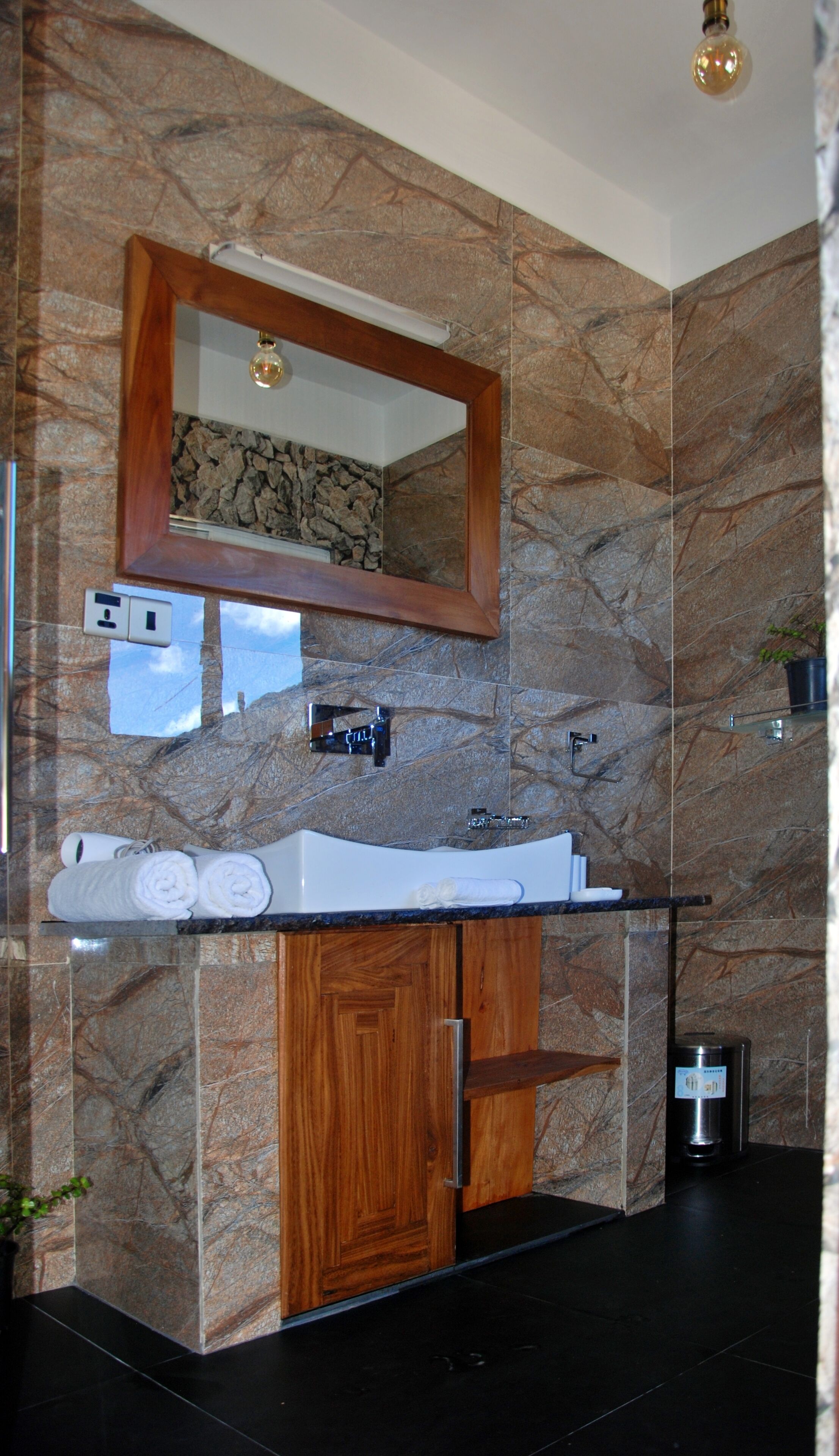 A bathroom with a marble wall, a wooden cabinet, a sink, and a mirror.