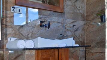 A bathroom with a marble wall, a wooden cabinet, a sink, and a mirror.