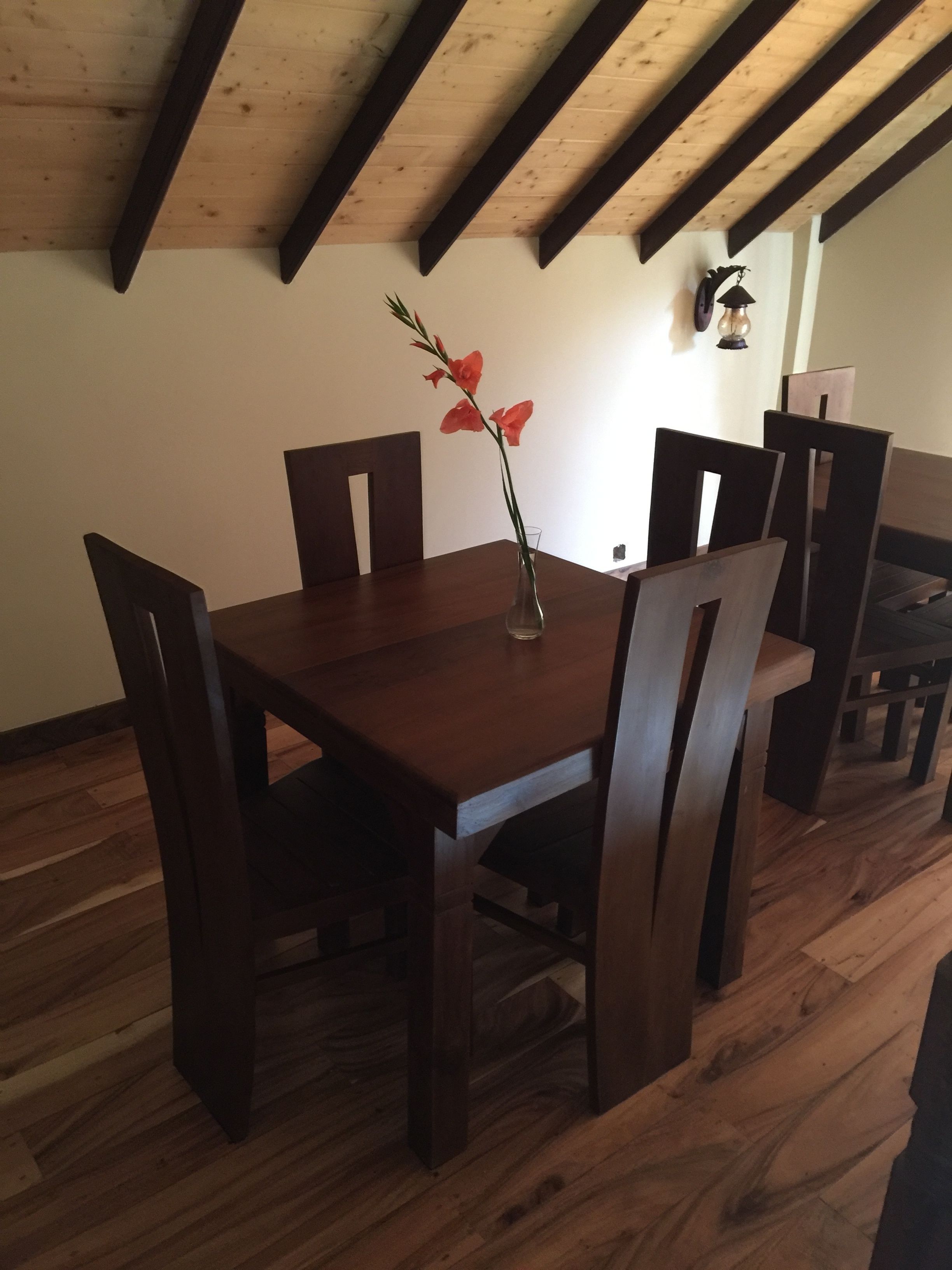 Zona pranzo con tavolo e sedie in legno, un vaso con fiori e un soffitto in legno con travi.