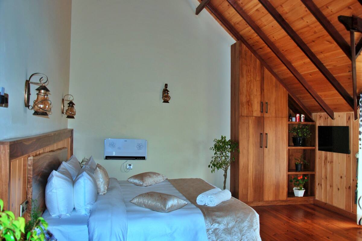 A bedroom with a wooden headboard, a bed with white and beige bedding, two wall-mounted lanterns, a wall-mounted air conditioner, and a wooden cabinet with shelves.