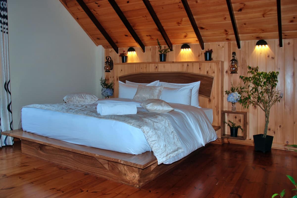 A wooden-framed bedroom with a large bed, built-in wall sconces, and potted plants.