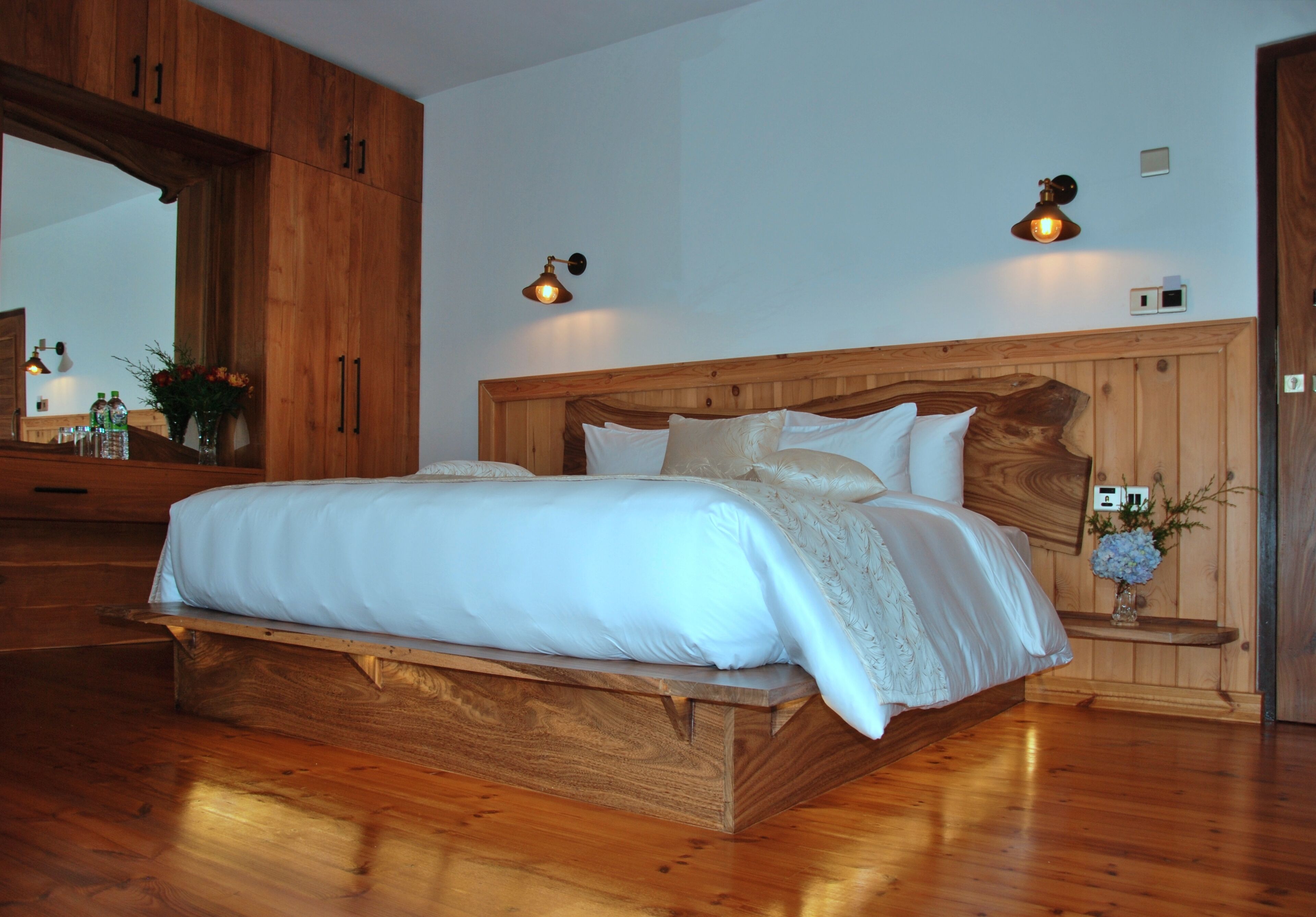 A wooden bed with a headboard, two bedside lamps, and a nightstand with a vase of flowers.