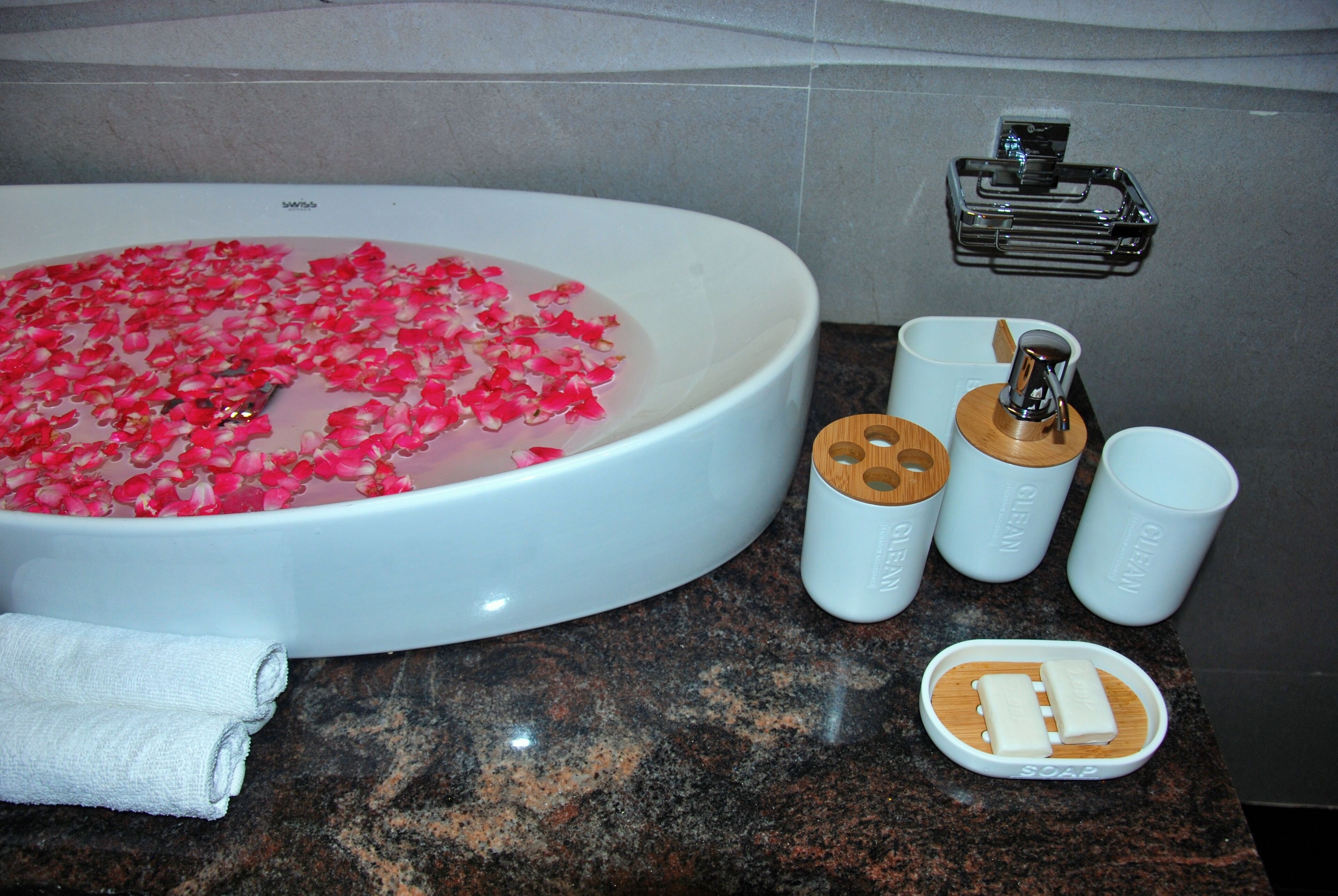 A bathroom with a large bathtub filled with rose petals, a towel, and toiletries including soap and cups.