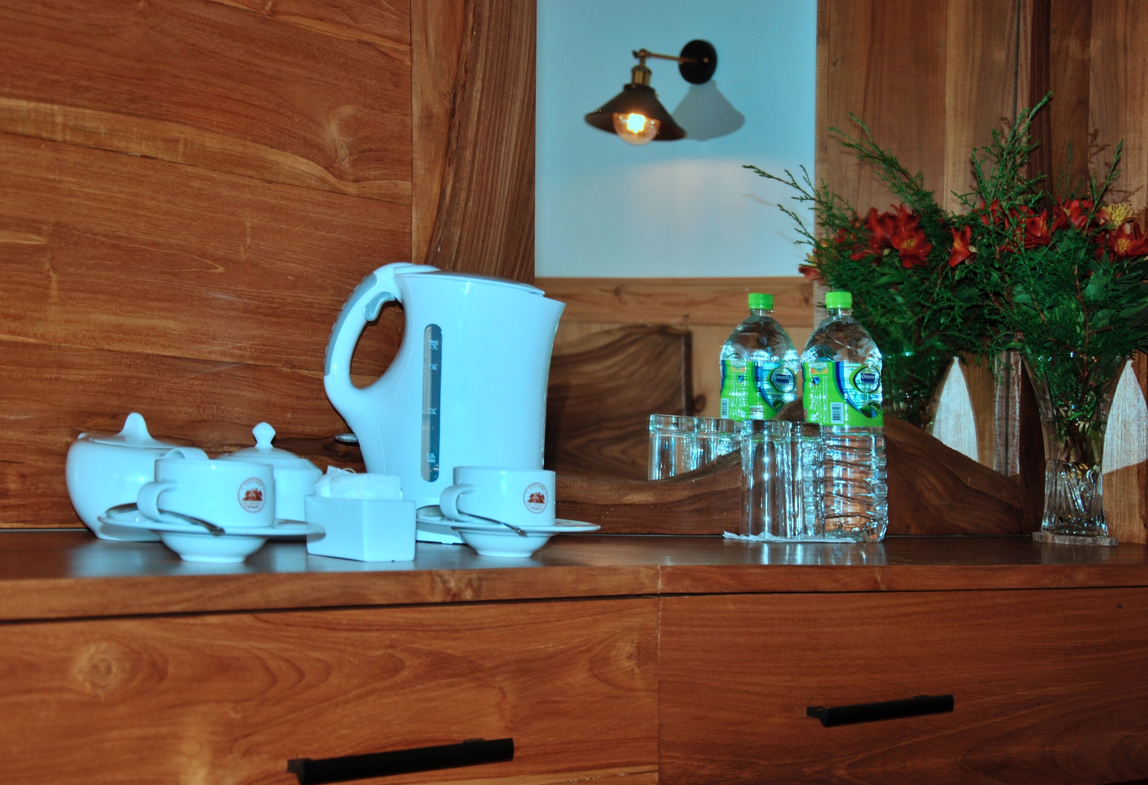 A wooden table with a white coffee maker, cups, and a vase with flowers.
