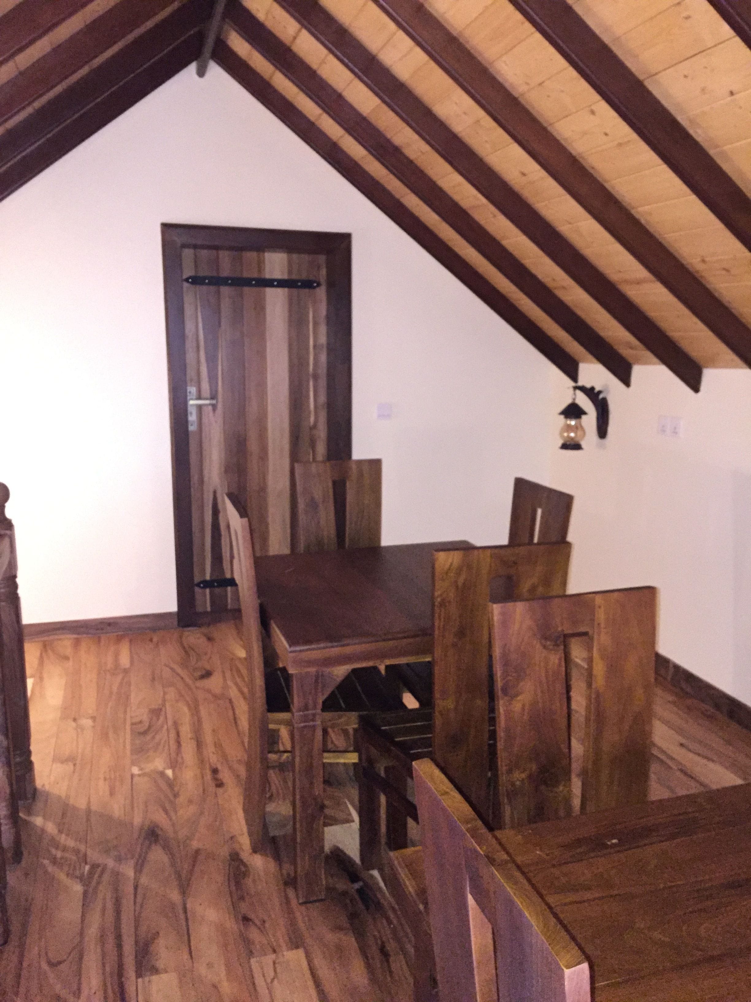 An attic room with a wooden dining table and chairs, a door, and a hanging light fixture.