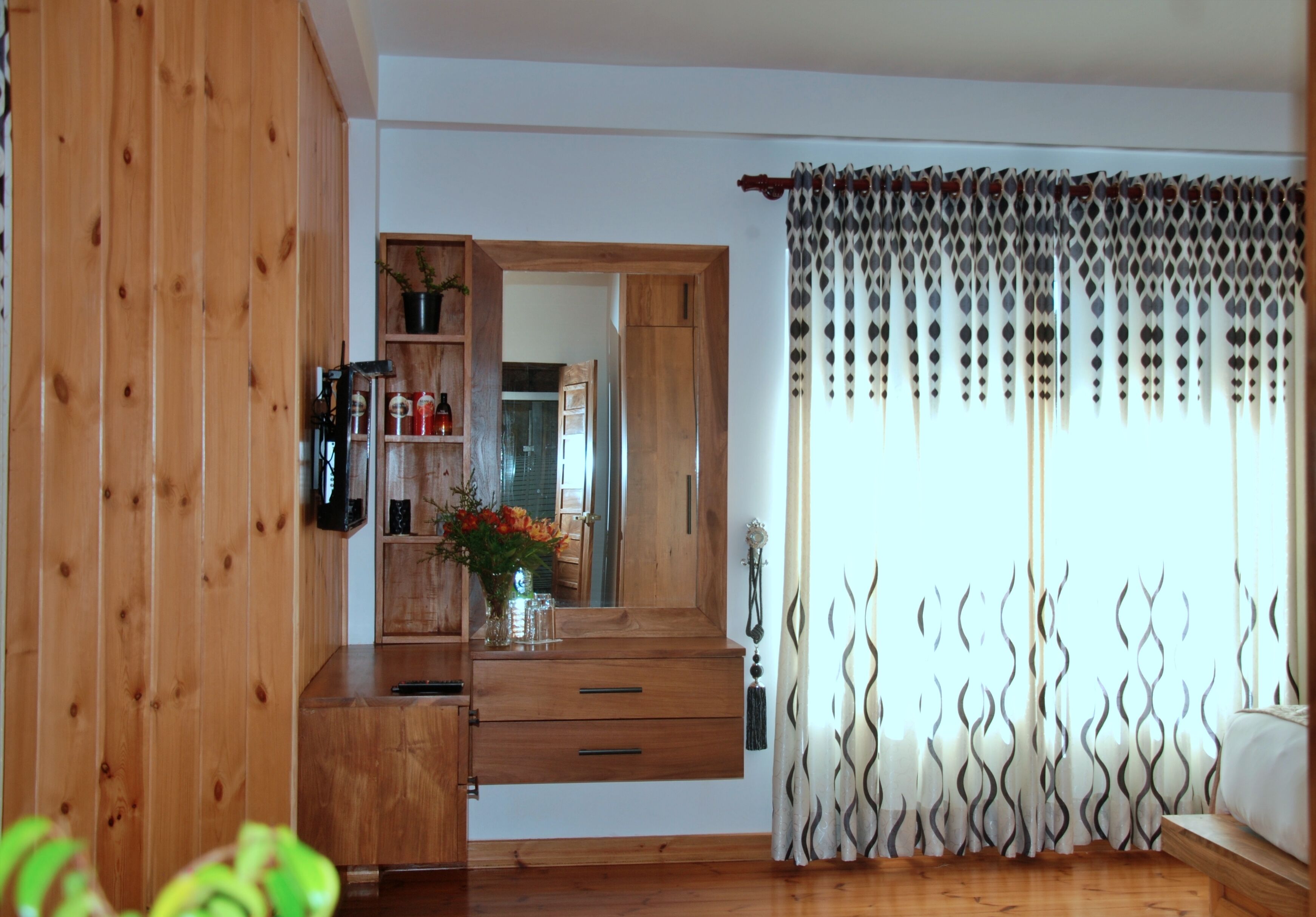 Ein Zimmer mit Holzwänden, einer Kommode mit Schubladen, einem Spiegel und einem Fenster mit gemusterten Vorhängen.