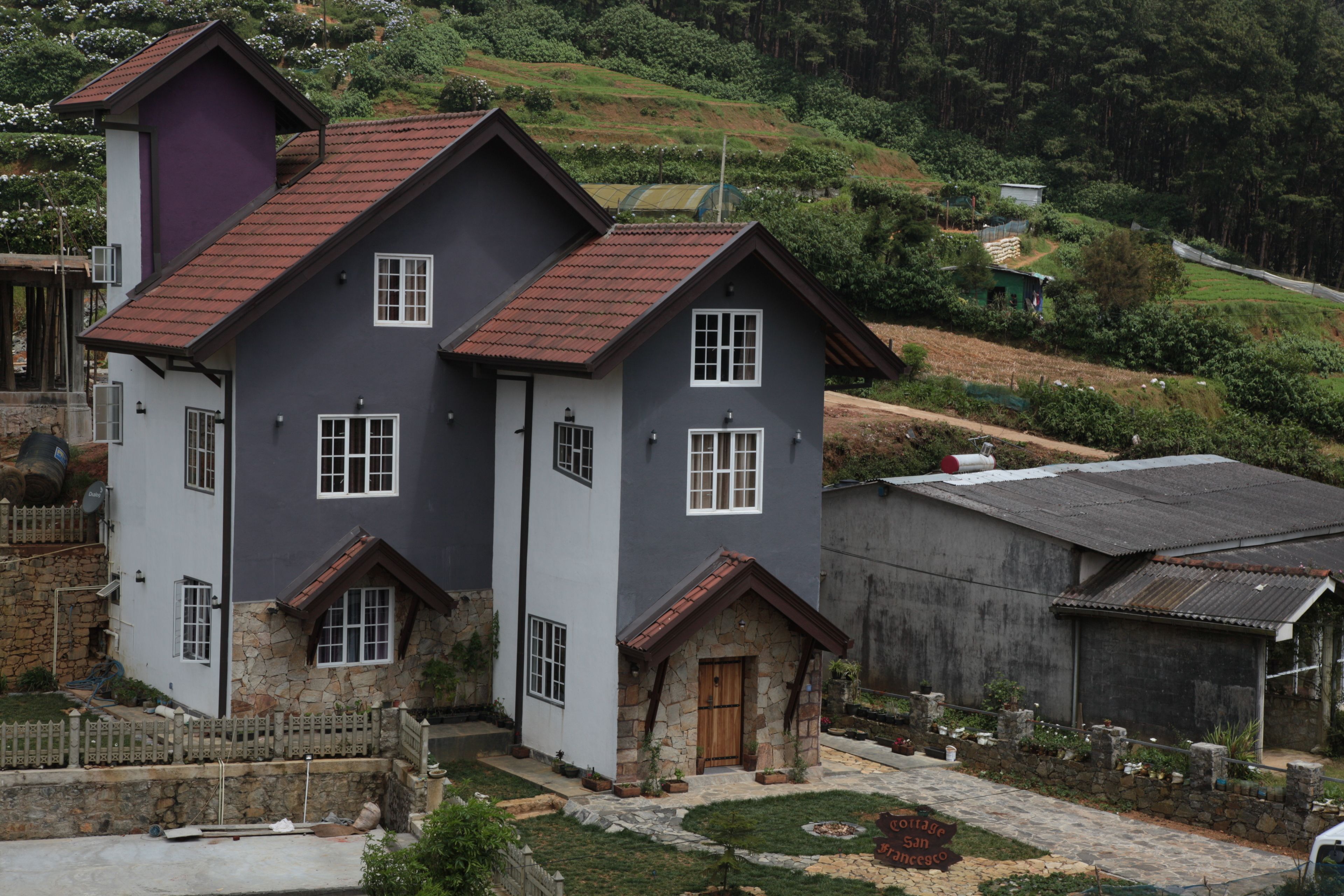 A two-story house with a stone foundation, a red-tiled roof, and a small front porch.