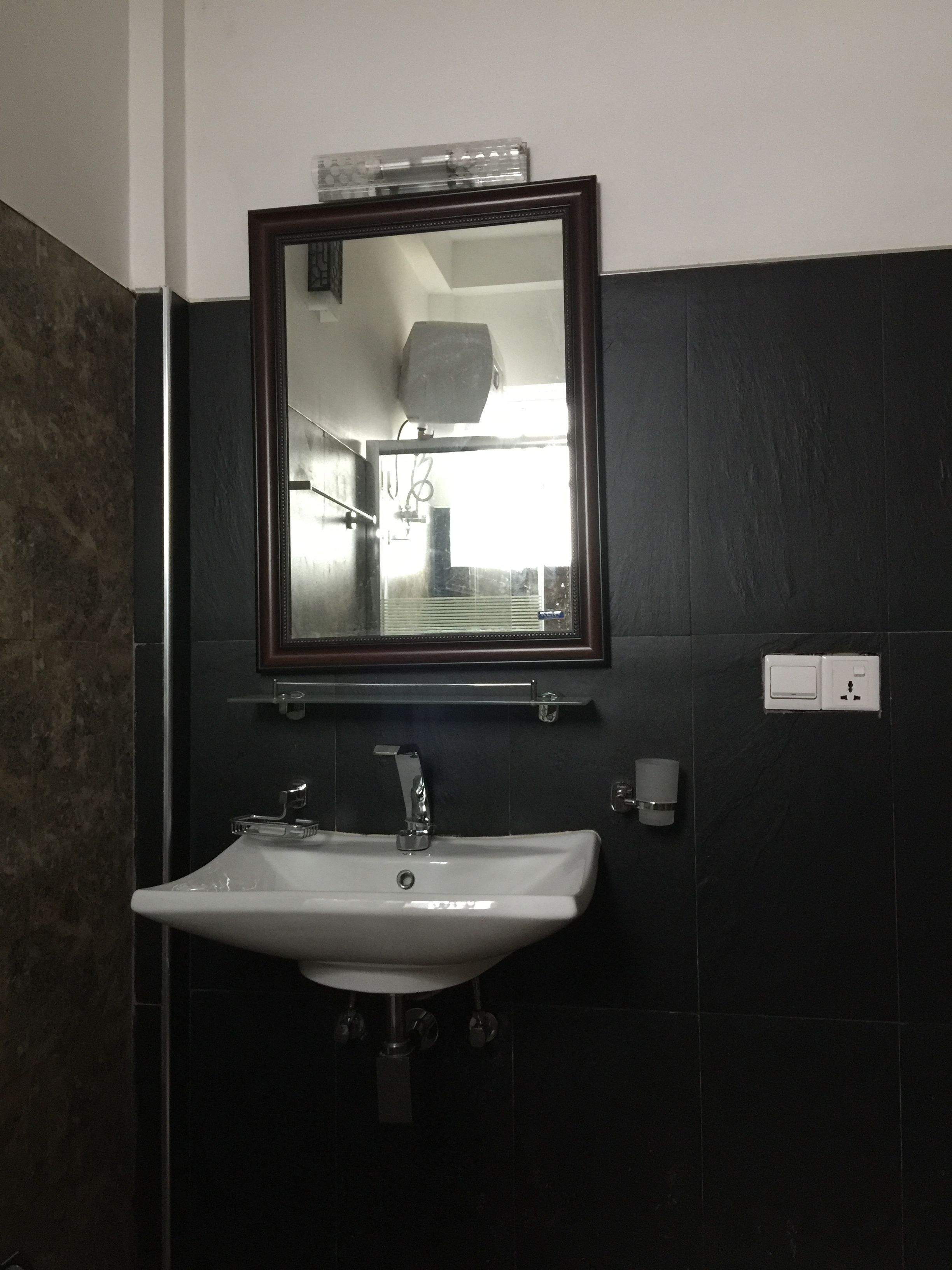 A bathroom with a white sink, a mirror above it, and a dark tiled wall.