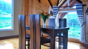 A wooden dining table with chairs, a vase with flowers, and a view of a green landscape through a window. - Cottage San Francesco (Nuwara Eliya)