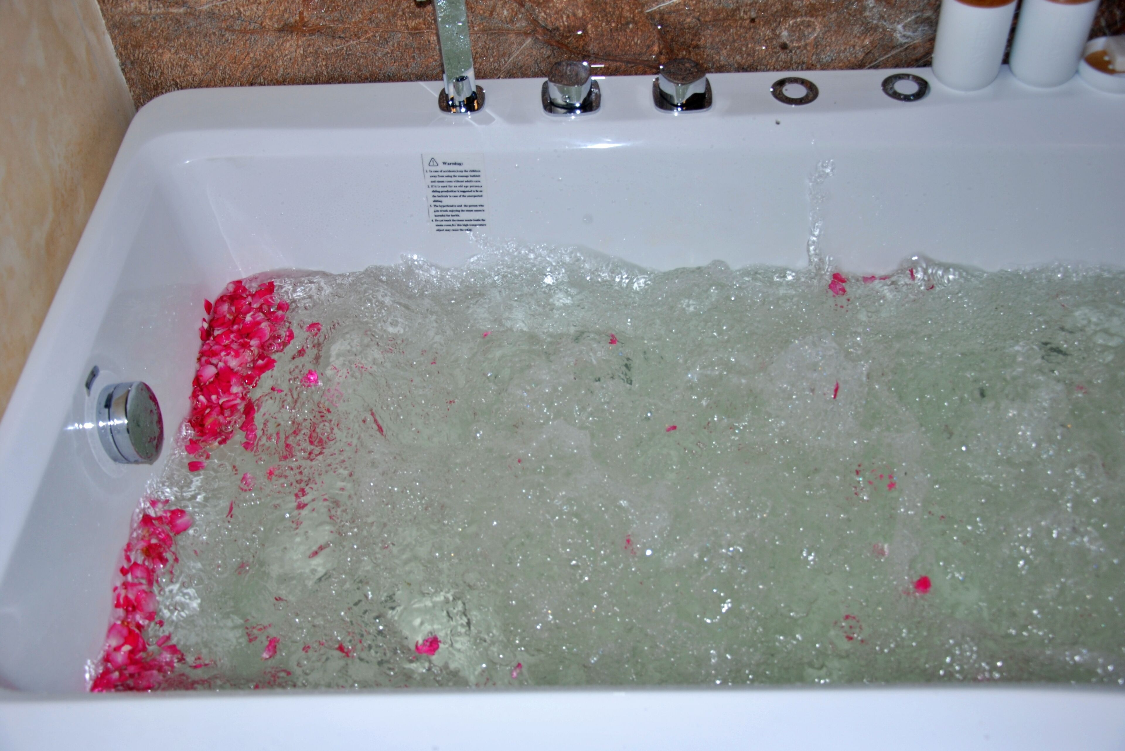Una bañera con agua corriente y pétalos de rosa.