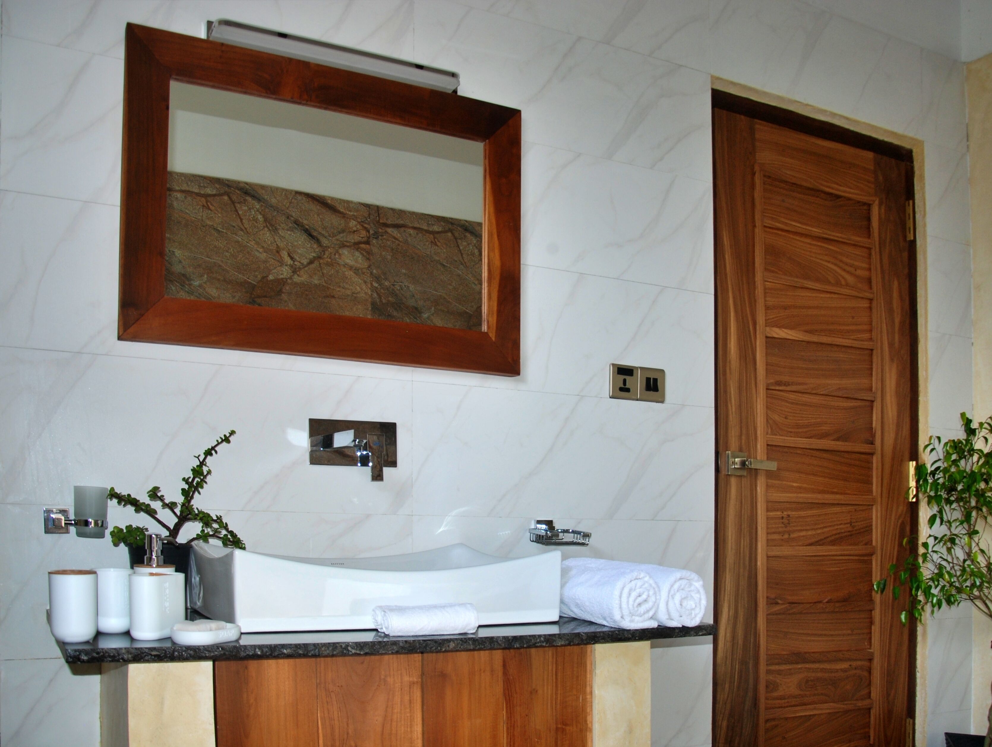 Un baño con lavamanos de mármol, tocador de madera, un espejo y una puerta de madera.