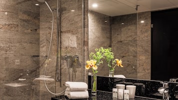 A modern bathroom with a glass-enclosed shower, marble walls, a black countertop, and a mirror.