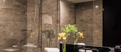 Un baño moderno con ducha envuelta en vidrio, paredes de mármol, encimera negra y un espejo.