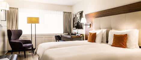 A hotel room with a large bed, a desk, a chair, and a lamp.