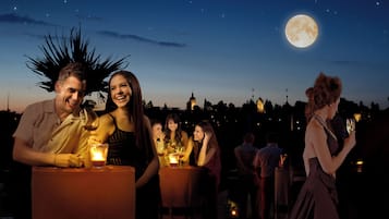 A group of people enjoying drinks at an outdoor evening event with a large moon in the sky.