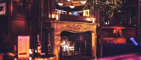 A warmly lit interior with a fireplace, a chandelier, and a potted plant.
