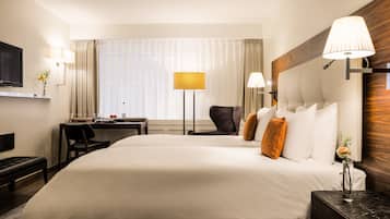 A hotel room with a large bed, a desk, a chair, a TV, and a window with curtains.