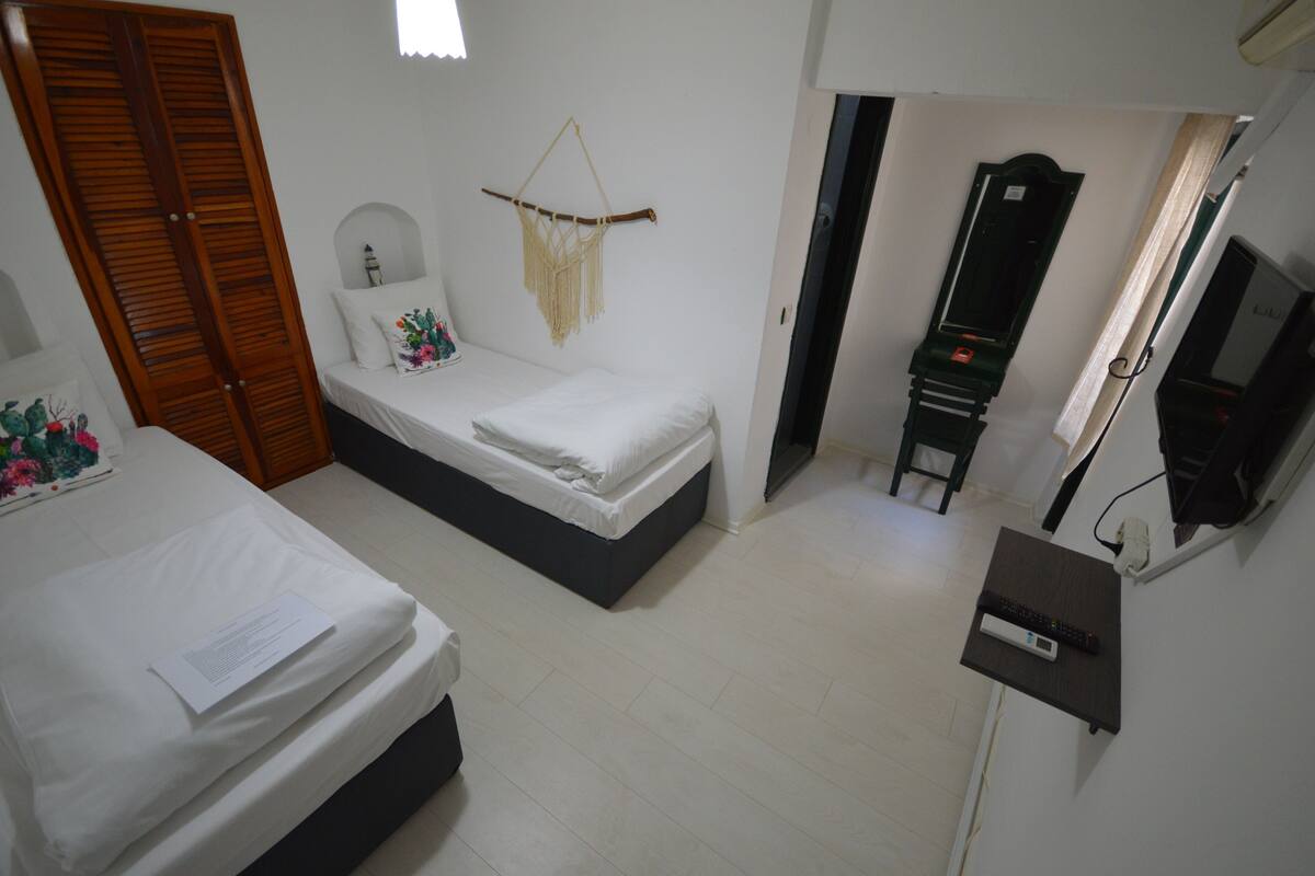 A bedroom with two beds, a wooden wardrobe, a wall-mounted TV, and a small desk with a remote control.