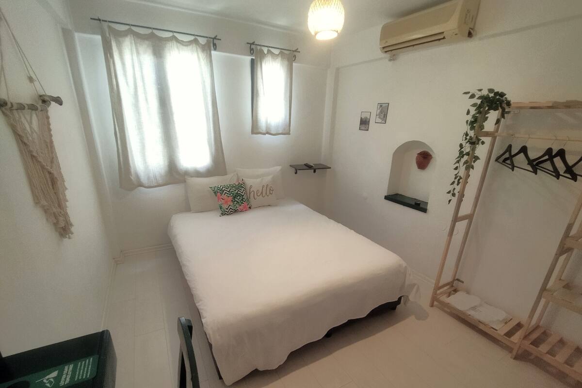 A bedroom with a bed, curtains, a shelf, a wall-mounted plant, and a ladder.