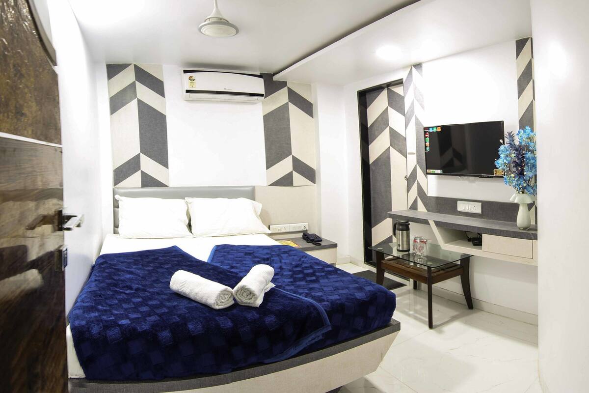 A modern hotel room with a bed, a desk, a TV, and an air conditioning unit.