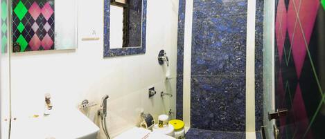 Un baño con un lavamanos blanco, un inodoro y una zona de ducha con azulejos estampados en azul y negro.