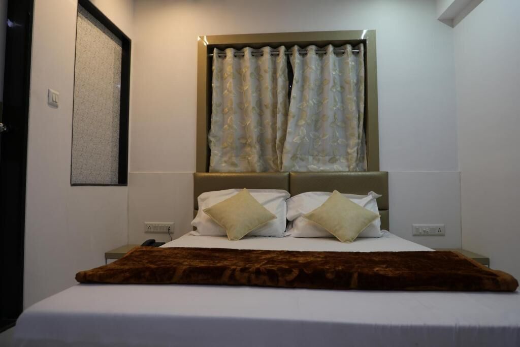 Habitación de hotel con cama, cabecera, ventana con cortinas y lámpara de pared.