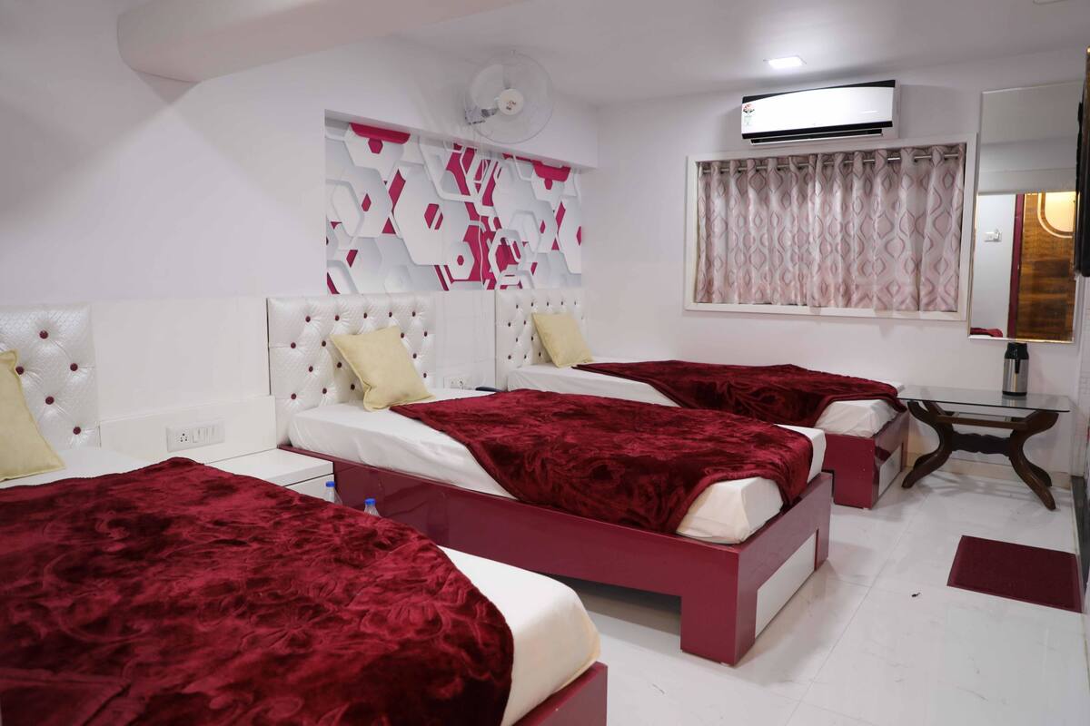 A hotel room with two beds, a bedside table, an air conditioning unit, and a window with curtains.