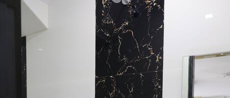 A bathroom with a black marble backsplash, a white sink, and a shower. There are two white containers with green lids on the counter.