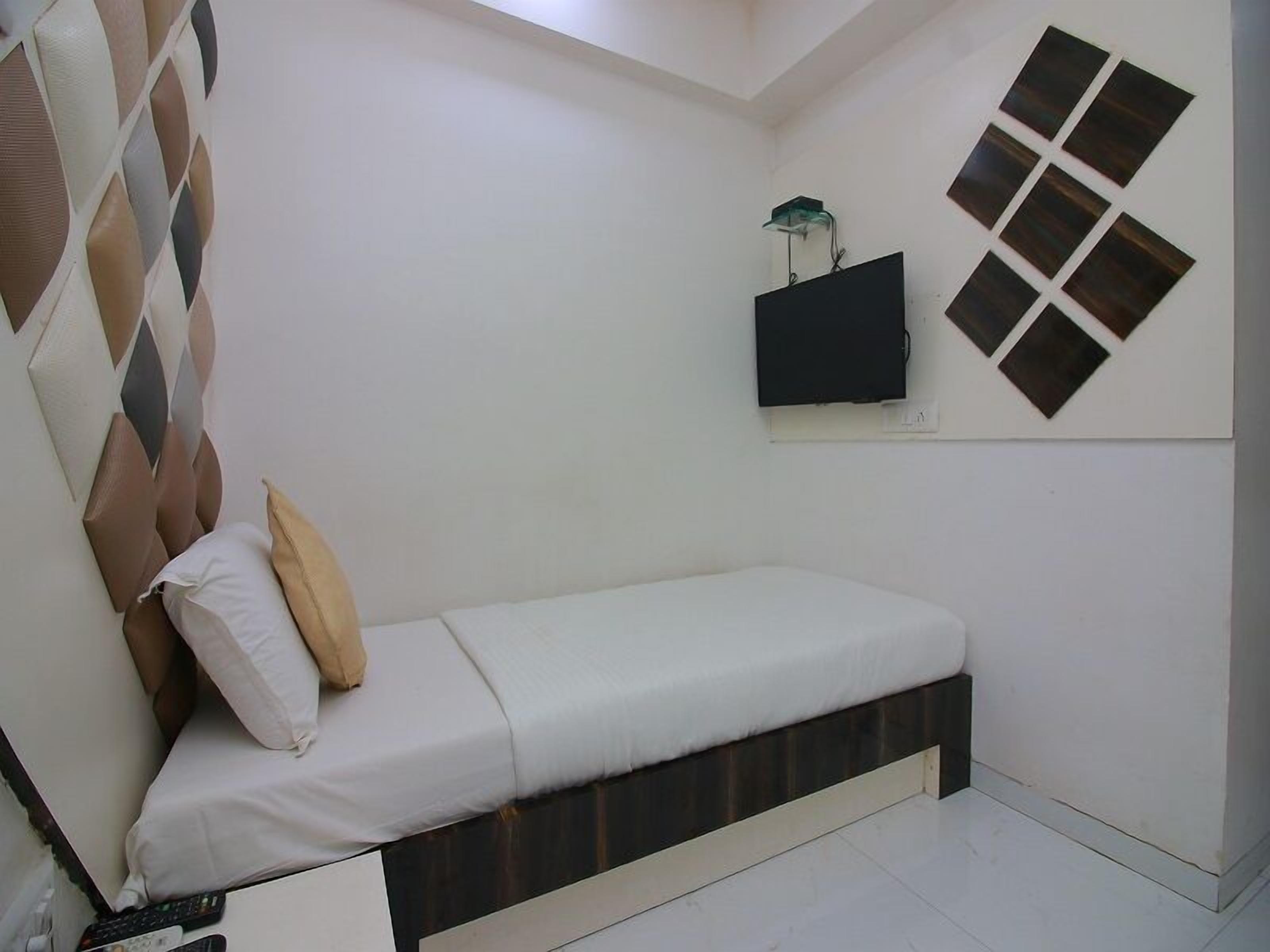 A small, neatly arranged bedroom with a bed, a TV mounted on the wall, and a decorative wall panel.
