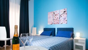 A hotel room with a bed, bedside tables, a table with a bottle of champagne and glasses, and a wall with a floral painting. - B&B Eternal Rome Inn (Rome)
