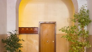 A hallway with a red carpet leading to a wooden door, flanked by potted plants and a tiled wall. - B&B Eternal Rome Inn (Rome)