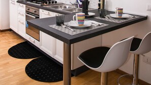 A modern kitchen with white cabinets, a black countertop, and two bar stools. - B&B Eternal Rome Inn (Rome)