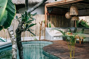 A pool area with a wooden deck, a thatched roof, and a seating area with cushions and a table. - MAJO Private Villas (Gili Trawangan)