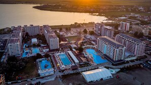 Ein Hotelkomplex mit mehreren Gebäuden, Swimmingpools und einem großen Wasserspiegel im Hintergrund.